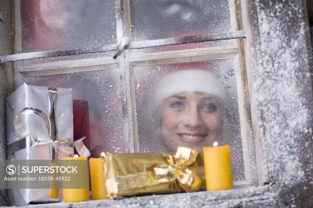 Austria, Salzburger Land, Young woman looking through window, parcels and candles on windowsill