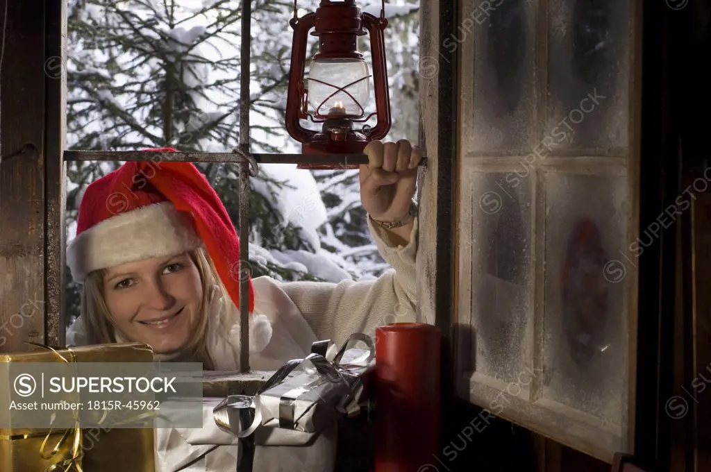 Austria, Salzburger Land, Woman with Santa's hat looking through window, Christmas parcels in foreground