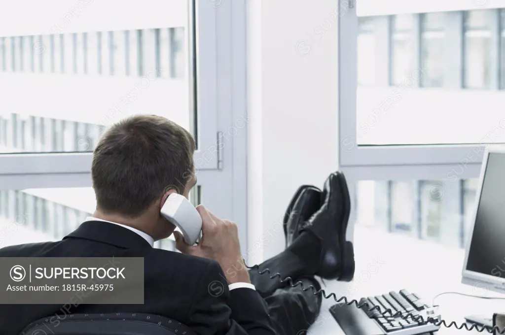 Businessman using phone in office, rear view