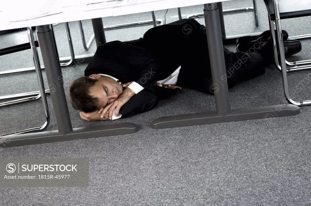 Businessman sleeping under desk