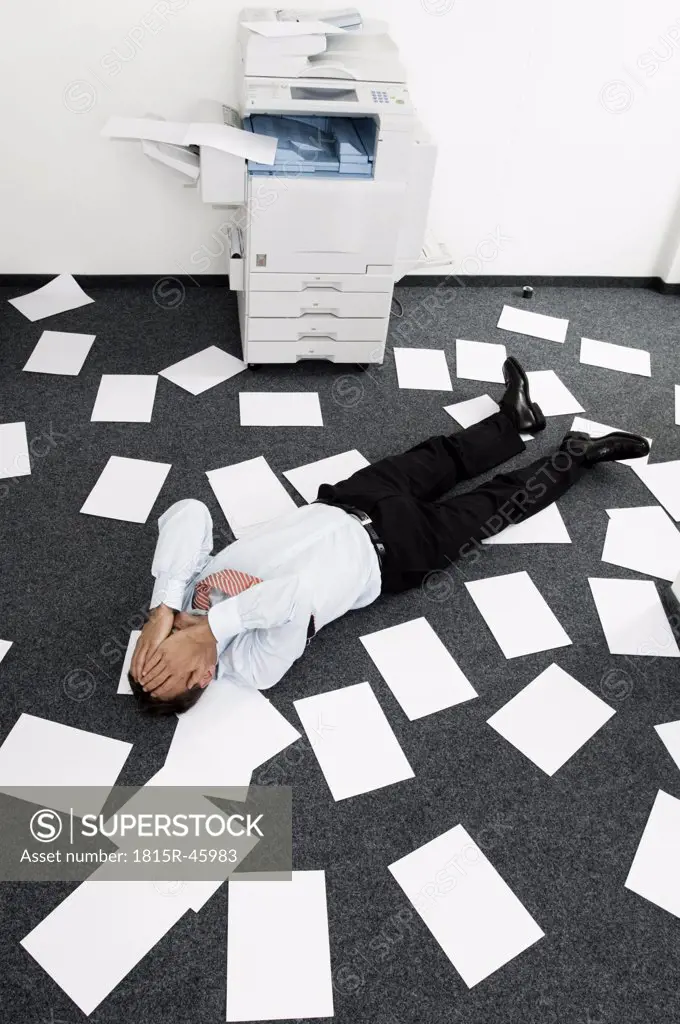 Businessman lying among slips of paper, hands to face