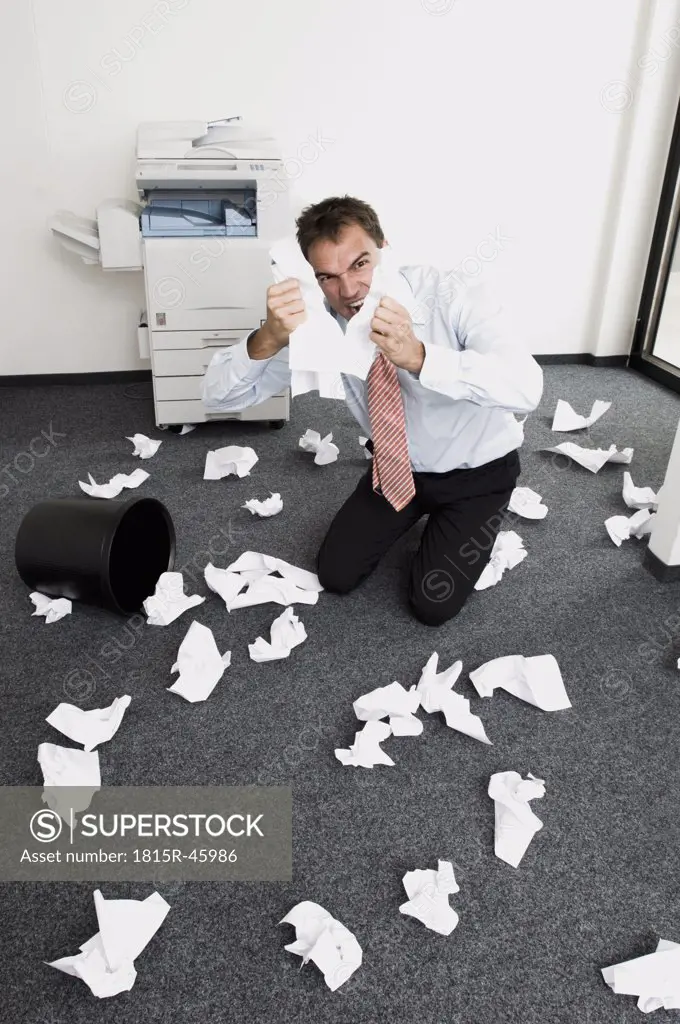 Businessman kneeling in despair, tearing sheets of paper