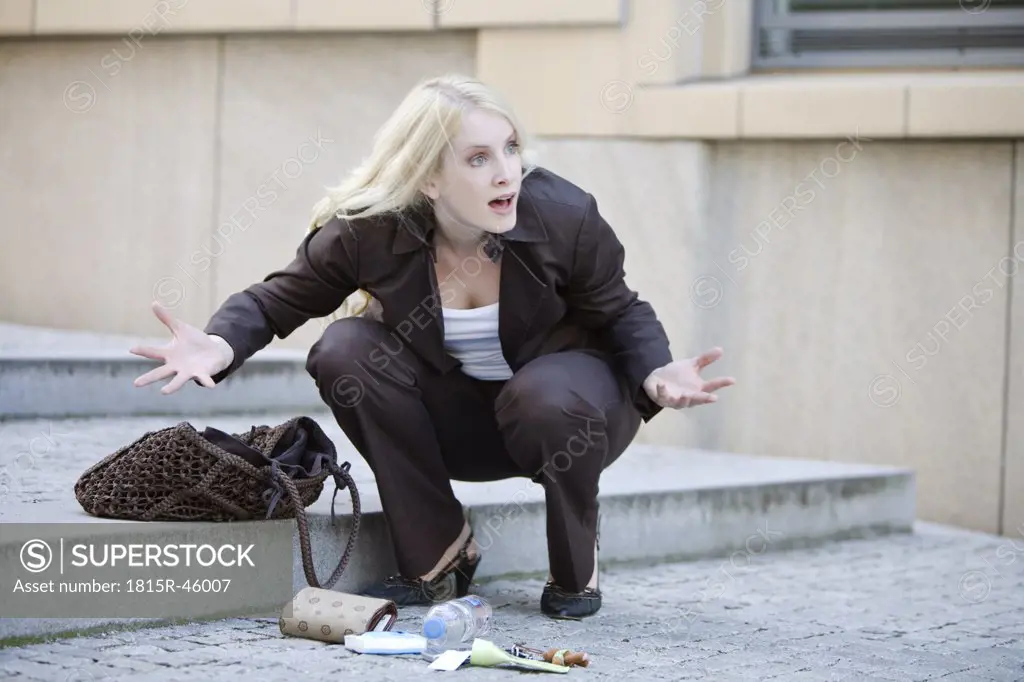 Young woman squatting next to handbag, gesturing helplessly