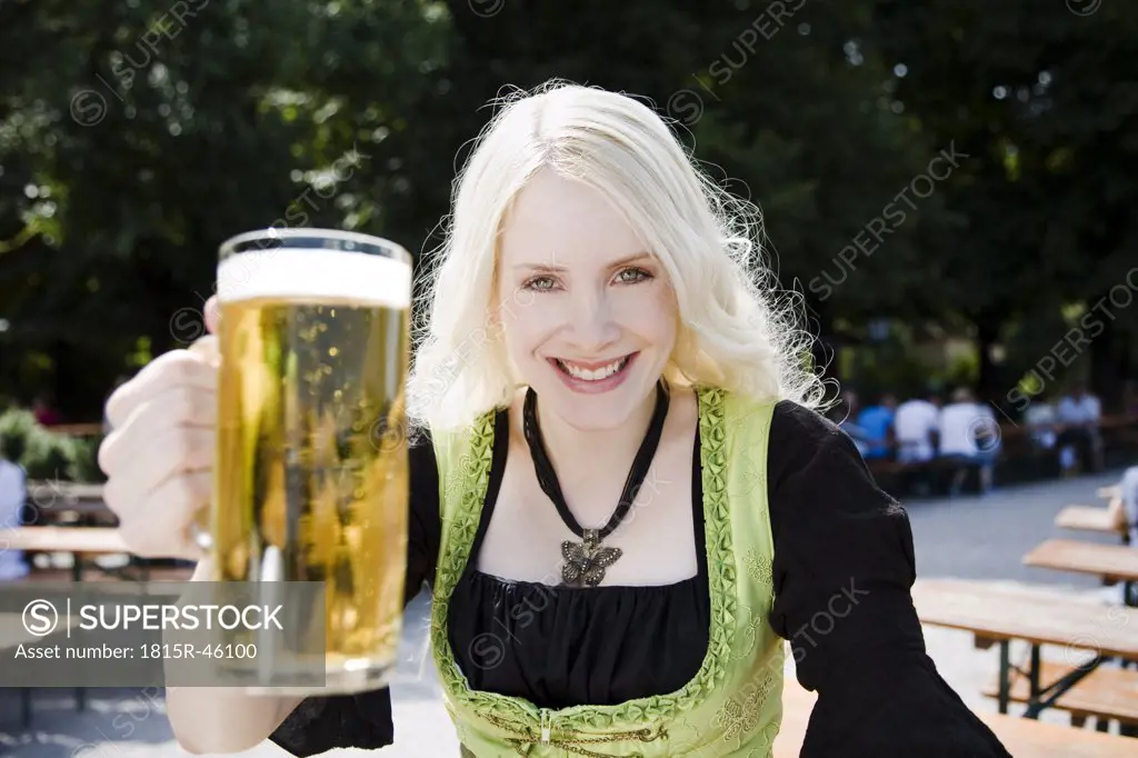 Germany, Bavaria, Munich, English Garden, Young woman holding beer stein, smiling, portrait