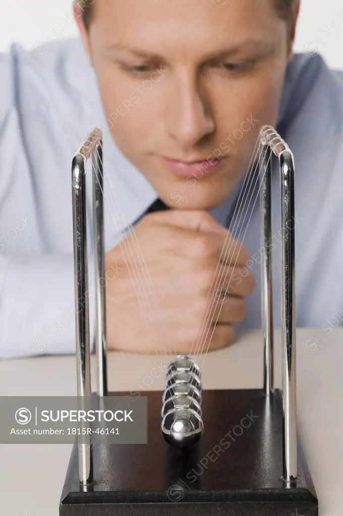 Businessman meditating, Newtons' Cradle in the foreground