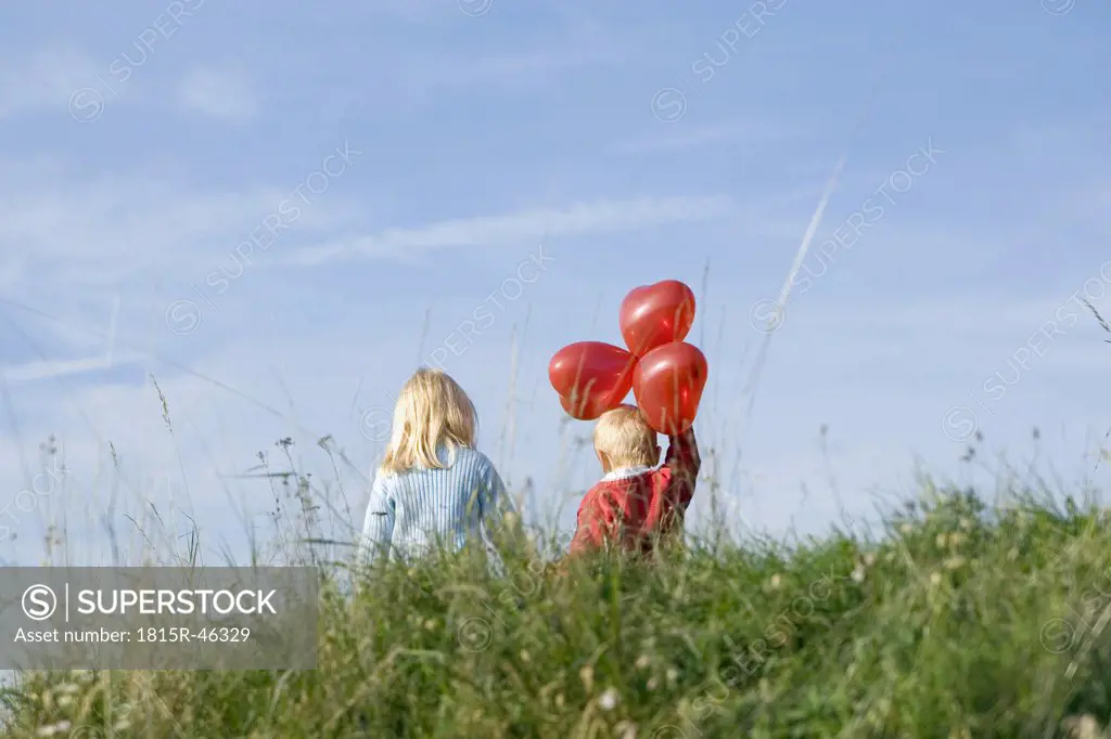Little girl and boy (3-4) with balloons walking hand in hand, rear view
