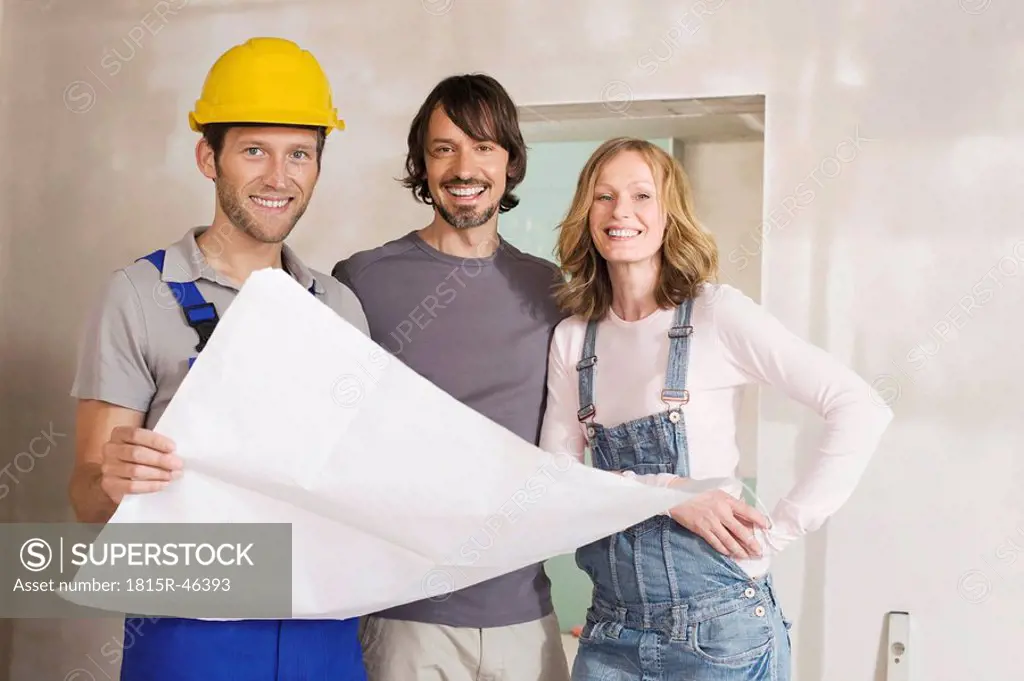 Young couple and construction worker holding construction plan, smiling, portrait