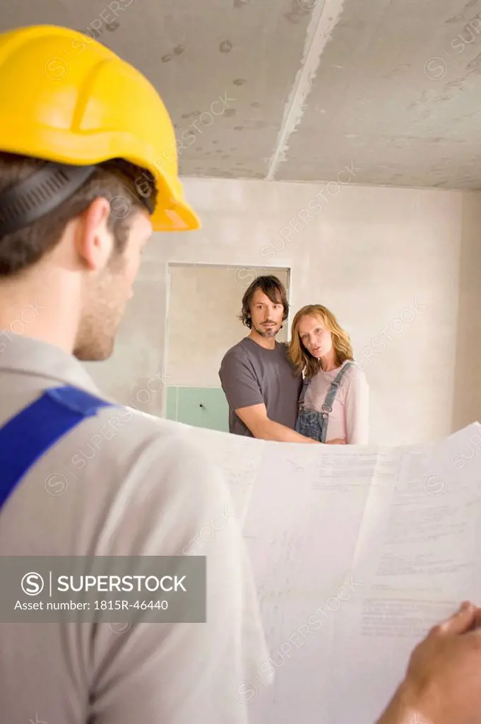 Construction worker holding construction plan, young couple in background