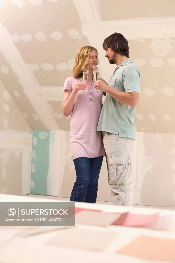 Young couple at construction site holding champagne glasses