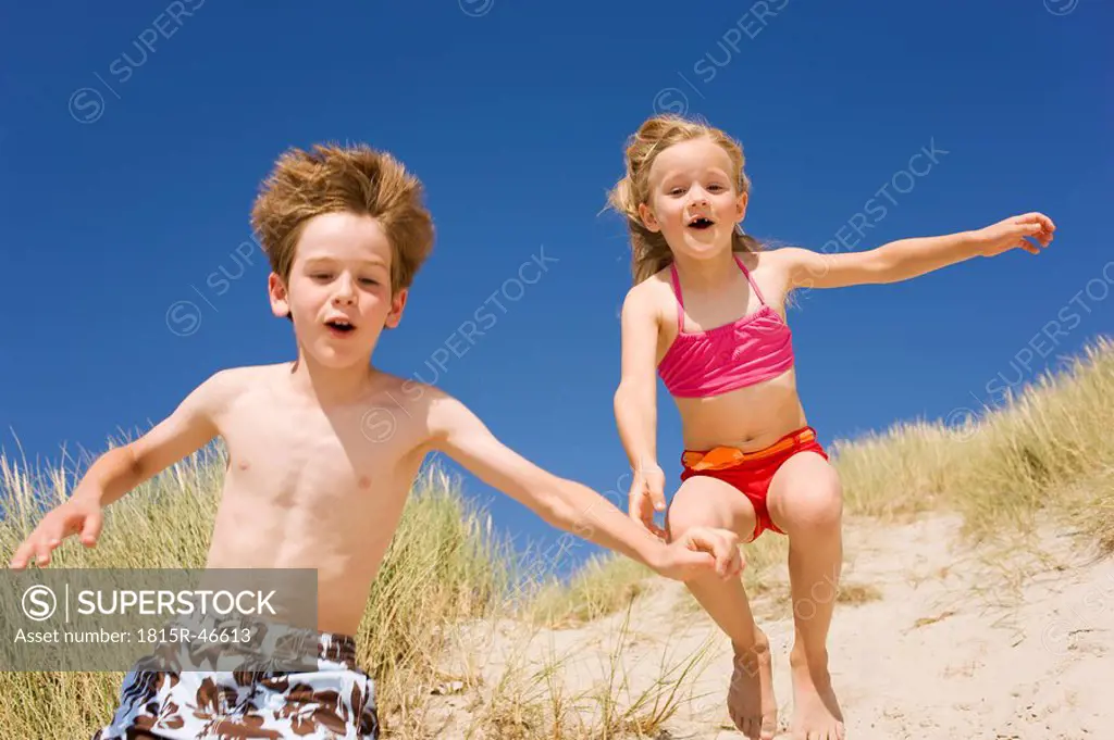 Germany, Baltic sea, Boy 8_9 and girl 6_7 jumping down beach dune
