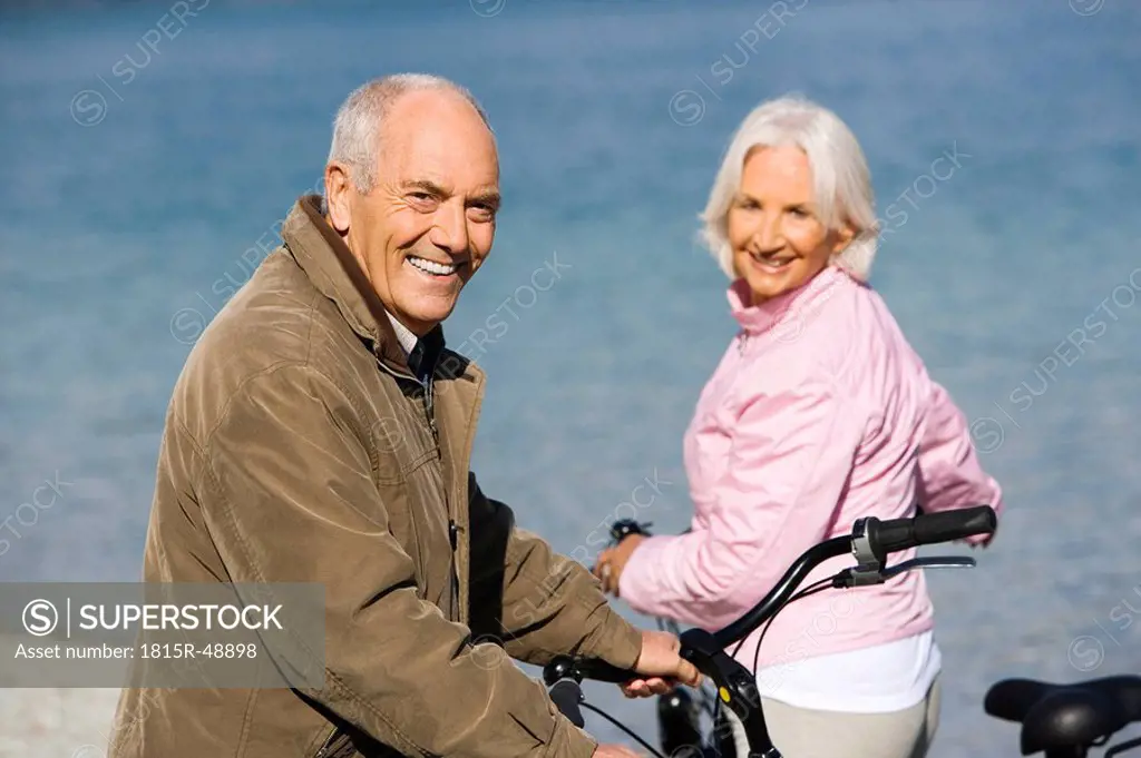 Germany, Bavaria, Walchensee, Senior couple pushing bikes across lakeshore
