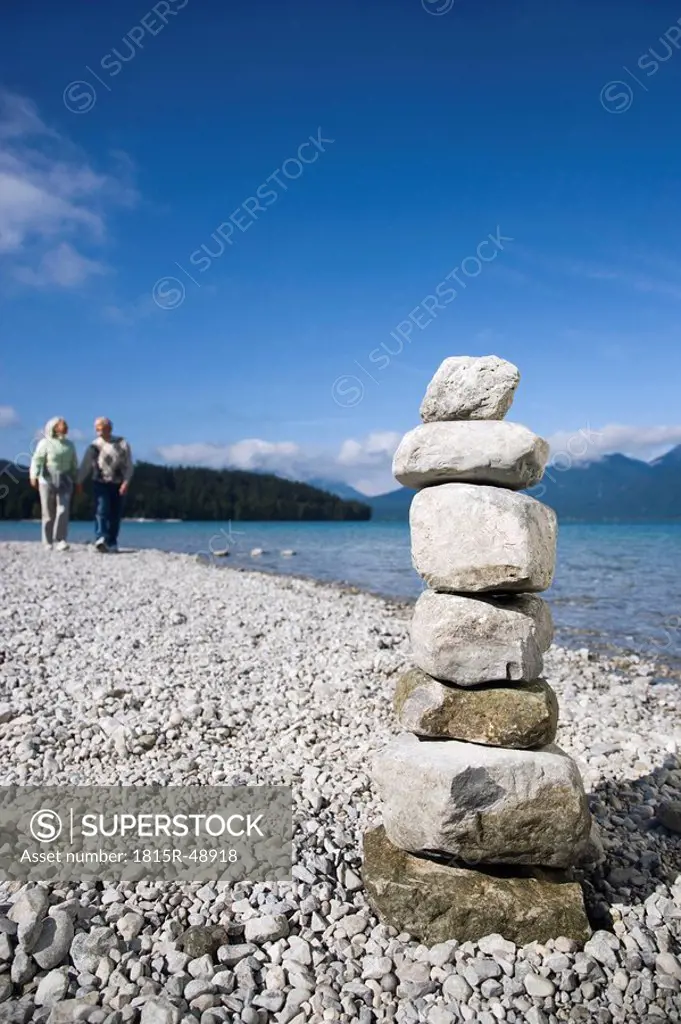 Germany, Bavaria, Walchensee, Senior couple taking a walk, stone pyramid in foreground