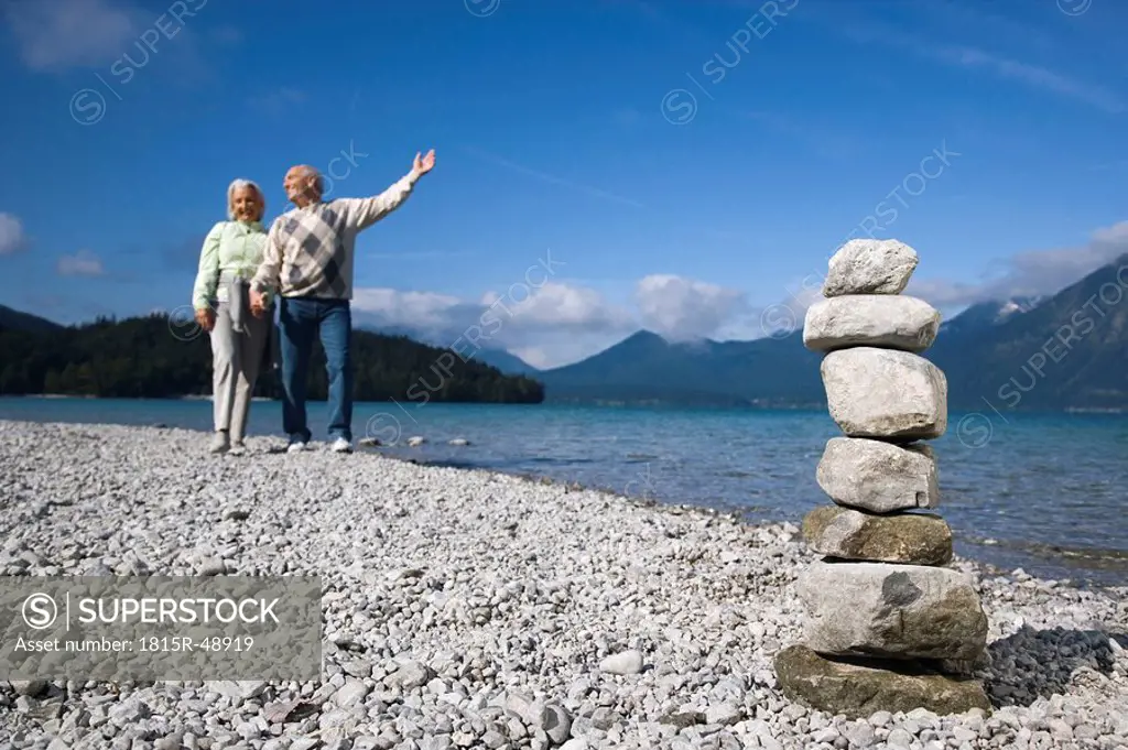 Germany, Bavaria, Walchensee, Senior couple taking a walk, stone pyramid in foreground