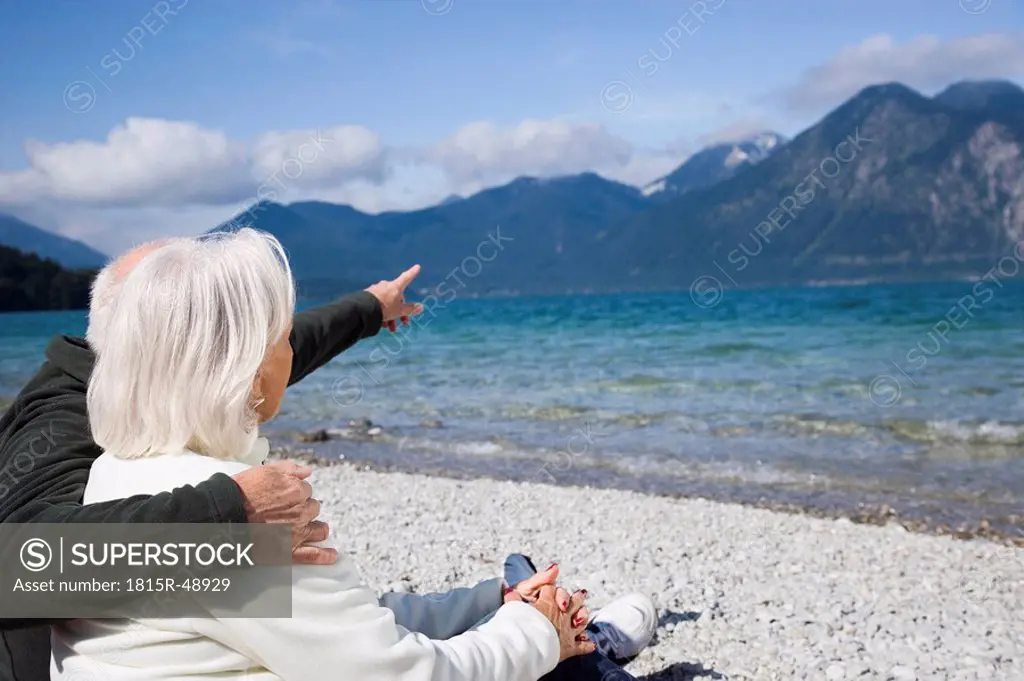 Germany, Bavaria, Walchensee, Senior couple relaxing on lakeshore, rear view