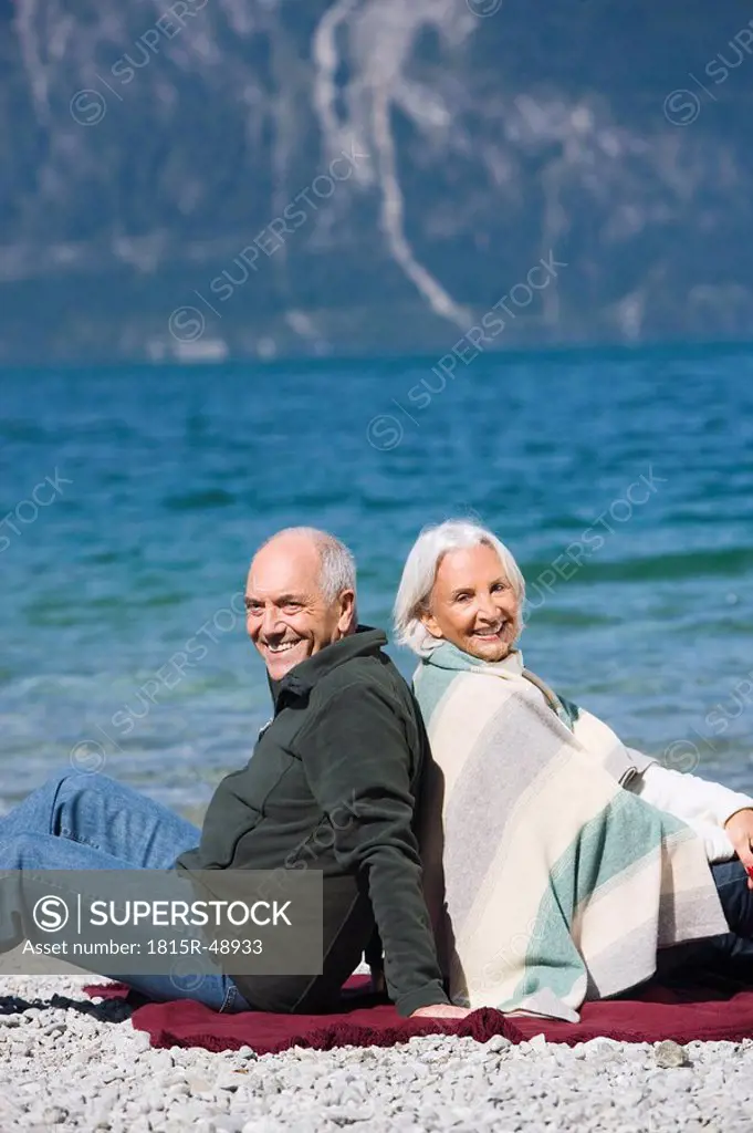 Germany, Bavaria, Senior couple relaxing on lakeshore, sitting back to back