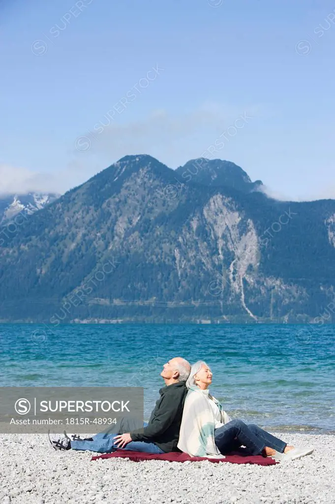 Germany, Bavaria, Senior couple relaxing on lakeshore, sitting back to back