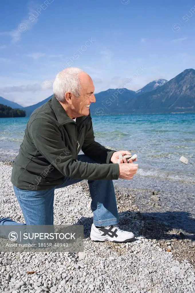 Germany, Bavaria, Walchensee, Senior man on lakeshore, about to skimming a stone