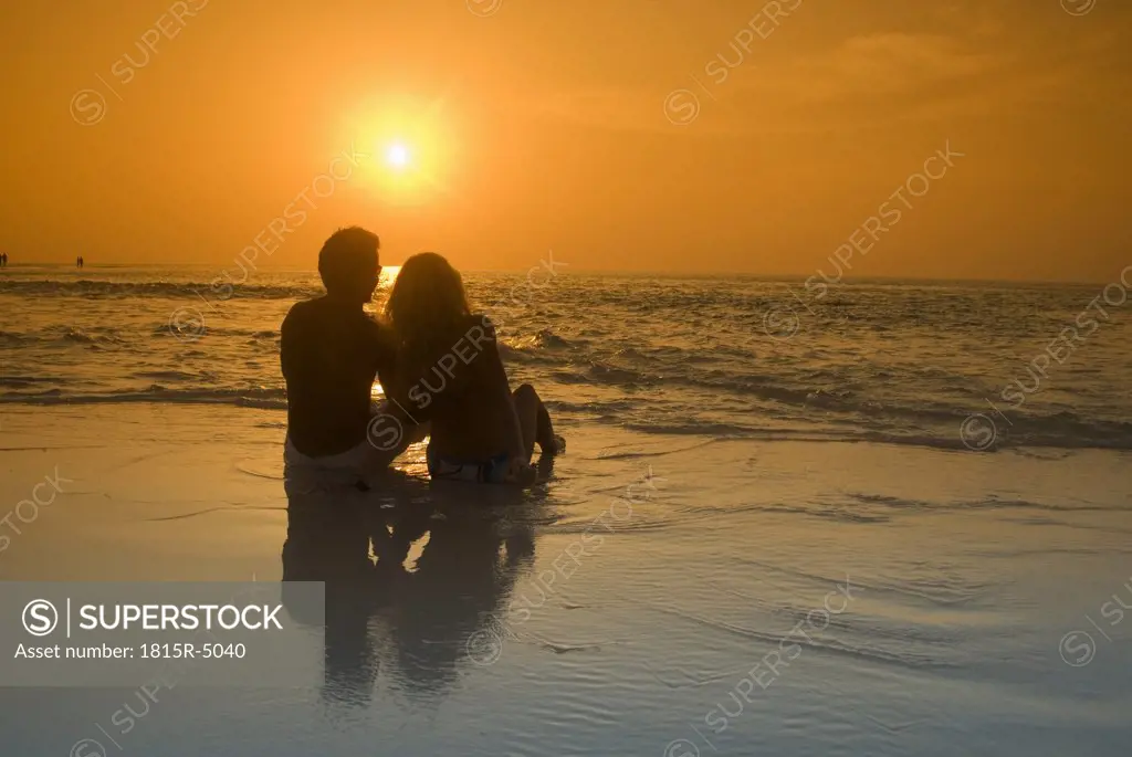 Couple sitting at the beach, silhouetted at sunset, Maldives