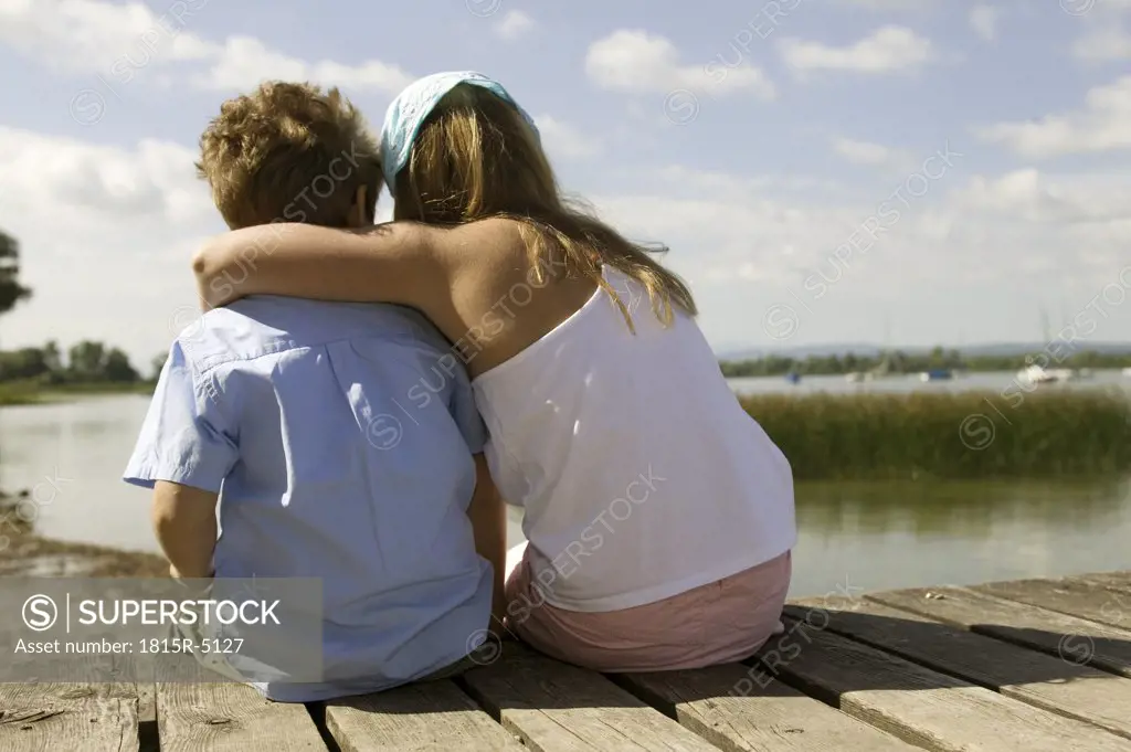 girl and boy sitting on a footbridge, rear view