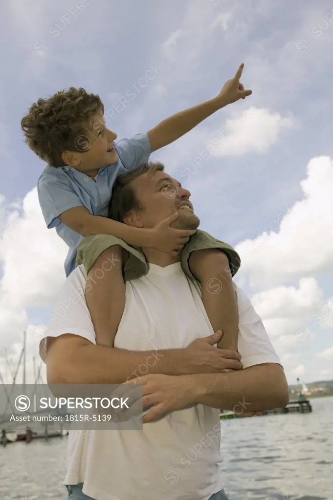 Father carrying boy (6-7) on shoulders, smiling, low angle view