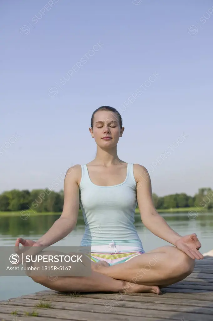 Woman (20-25) exercising yoga on jetty