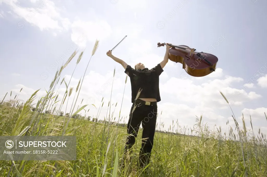 Young cellist in field, arms up