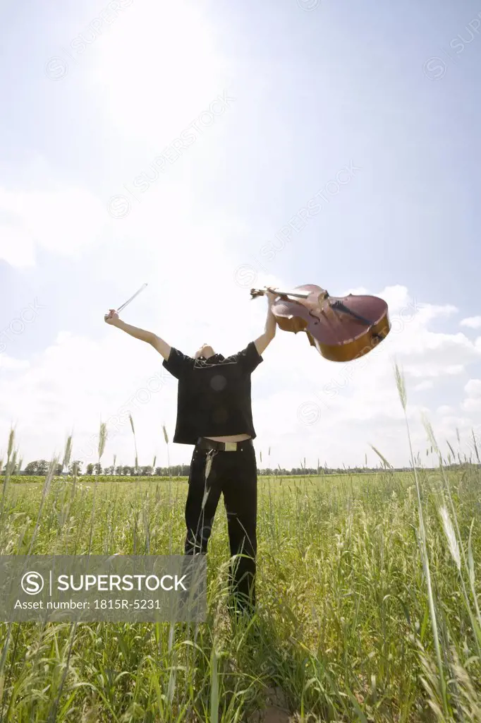 Young man standing in field with cello, arms out