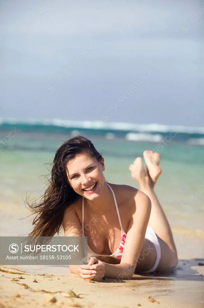Young woman lying on beach, smiling, portrait