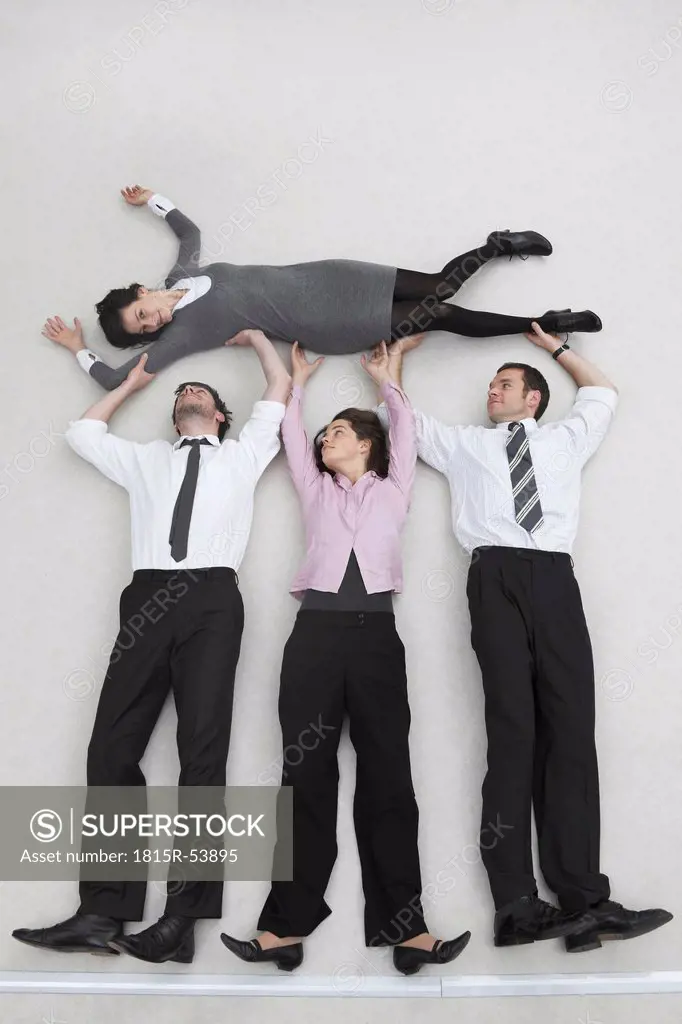 Four business people, businessmen and businesswoman lifting colleague, portrait, elevated view