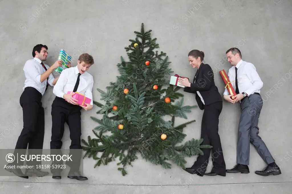 Four business people with Christmas presents standing round Christmas tree, elevated view
