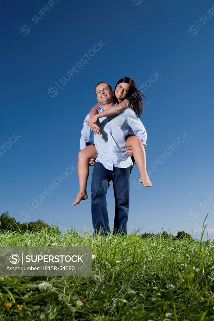 Young man carrying woman piggyback across meadow