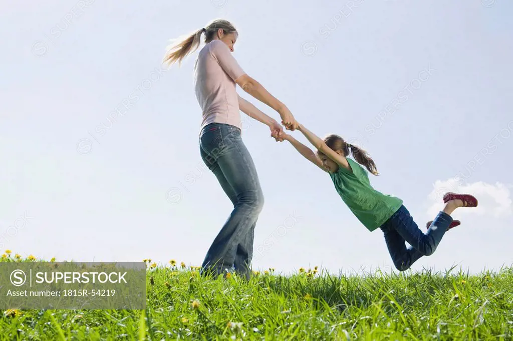 Germany, Bavaria, Munich, Mother swinging daughter 6_7 on meadow, fooling about