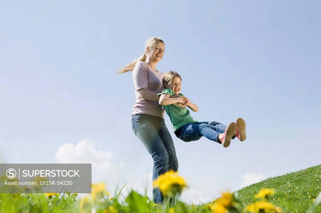 Germany, Bavaria, Munich, Mother swinging daughter 6_7 on meadow, fooling about