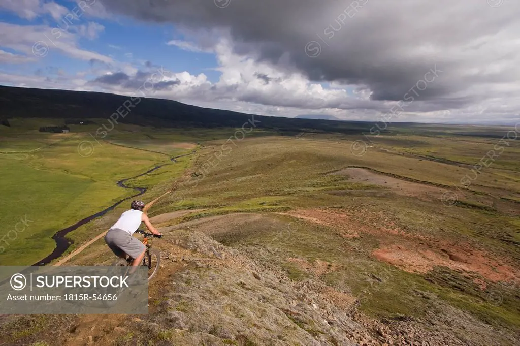 Iceland, Man mountain biking across hilly landscape