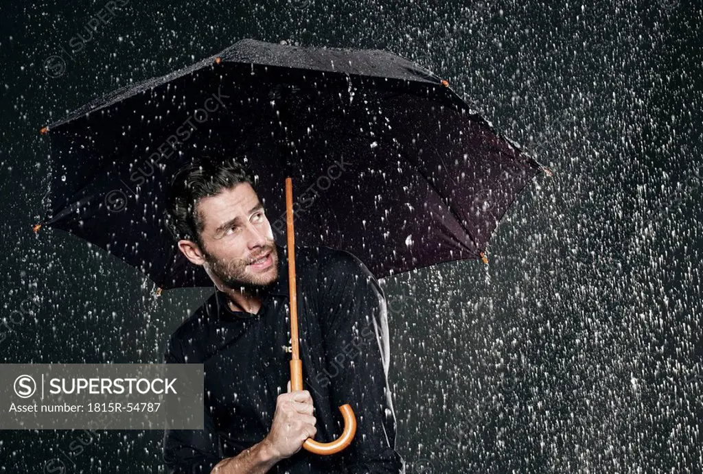 Man holding umbrella in rain, looking away.