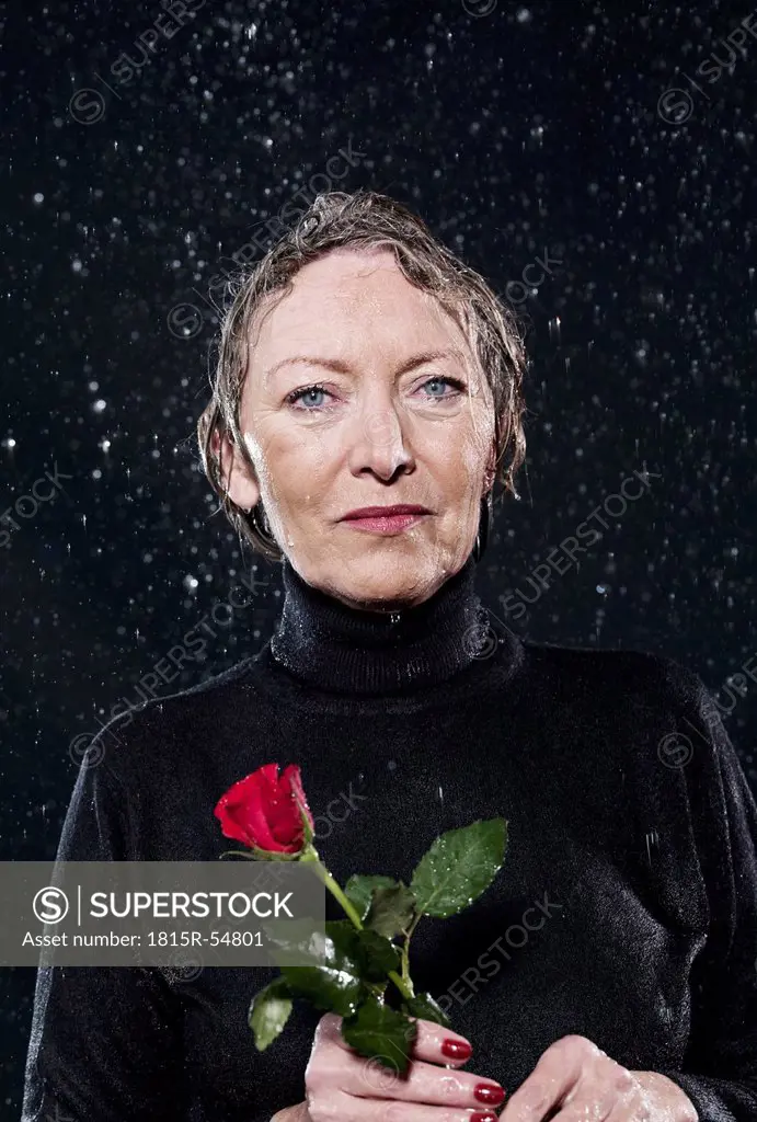 Woman standing in rain, holding rose.