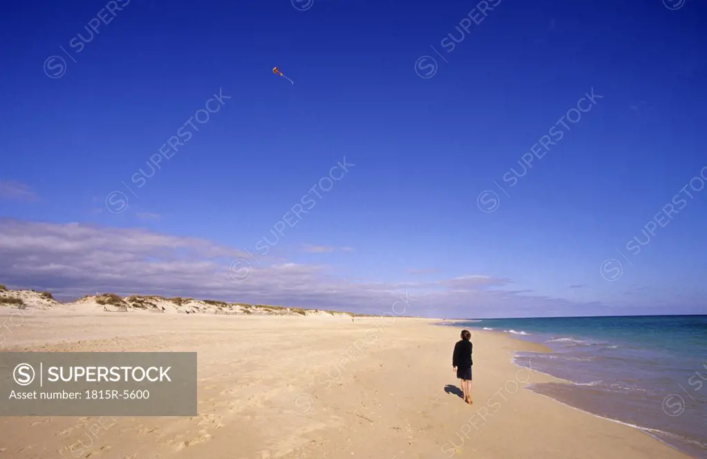Portugal, Algarve, boy (8-11) flying kite on beach, rear view