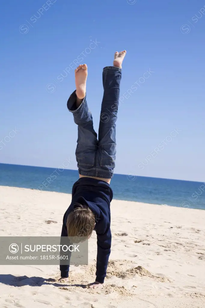 Portugal, Algarve, boy (8-11) doing handstand on beach, rear view