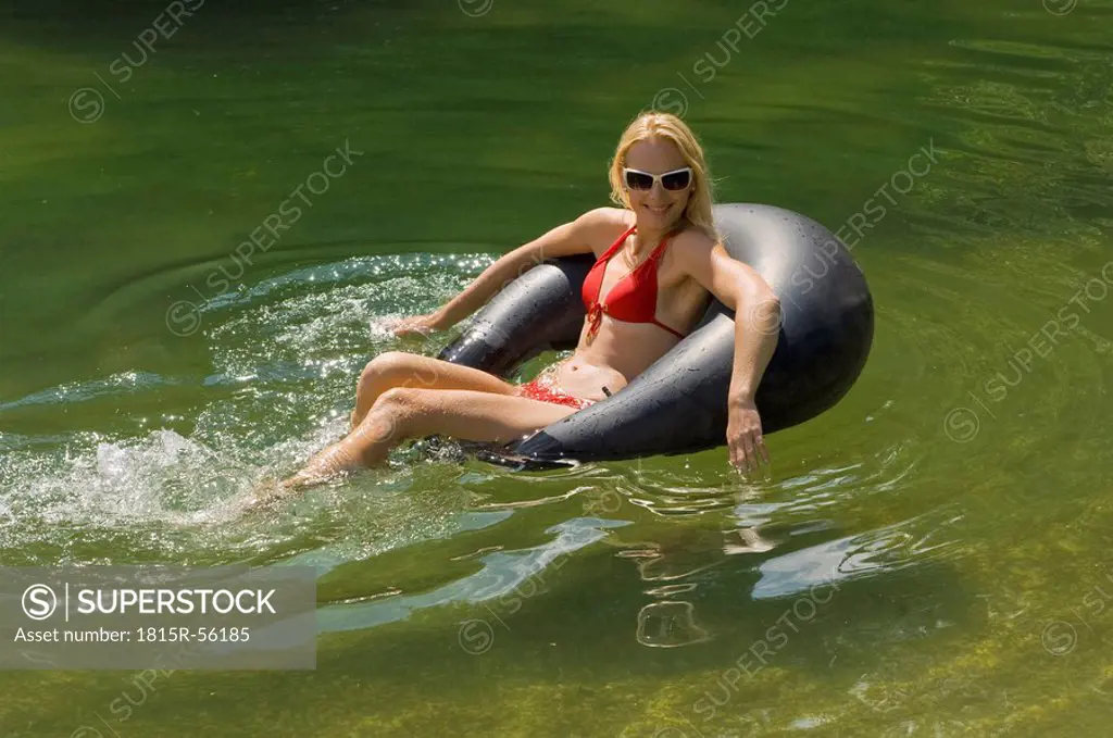 Austria, Salzburger Land, Lake Reitecksee, Young woman relaxing on floating tire