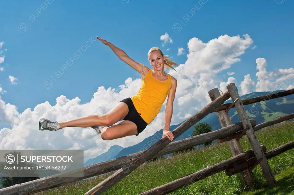 Austria, Salzburger Land, Young woman jumping over fence