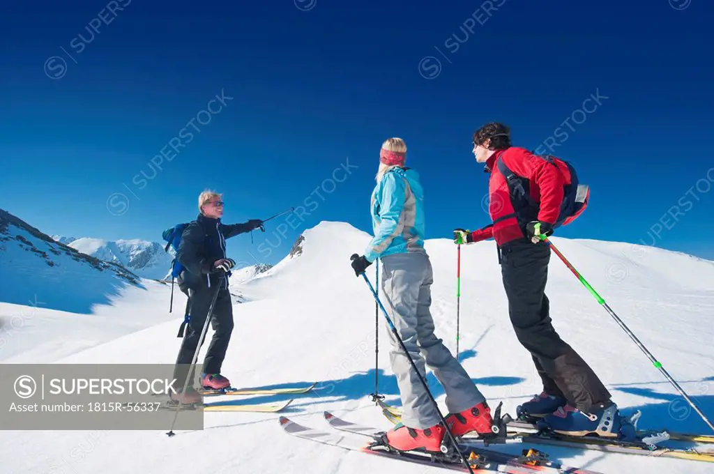 Austria, Salzburger Land, Altenmarkt, Zauchensee, Three persons cross country skiing in mountains, man pointing with ski pole