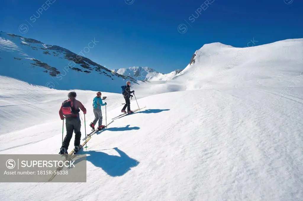Austria, Salzburger Land, Altenmarkt, Zauchensee, Three persons cross country skiing in mountains, rear view
