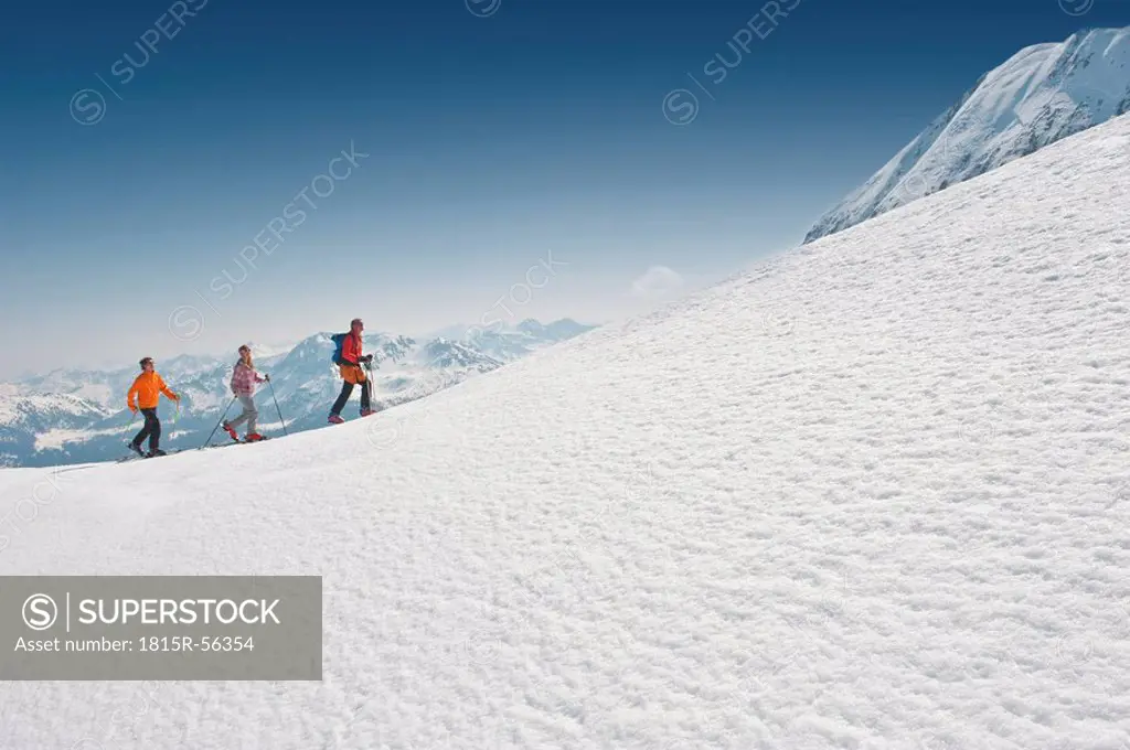 Austria, Salzburger Land, Altenmarkt, Zauchensee, Three persons cross country skiing in mountains, side view
