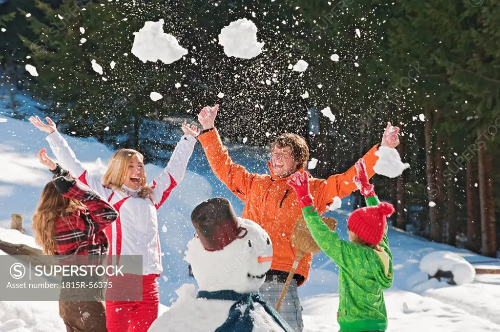 Austria, Salzburger Land, Altenmarkt, Family standing by snowman, throwing snow in the air, laughing, portrait