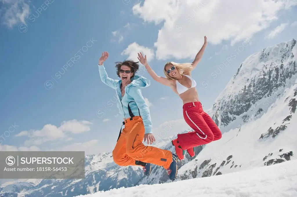 Austria, Salzburger Land, Young couple jumping in air, laughing, portrait