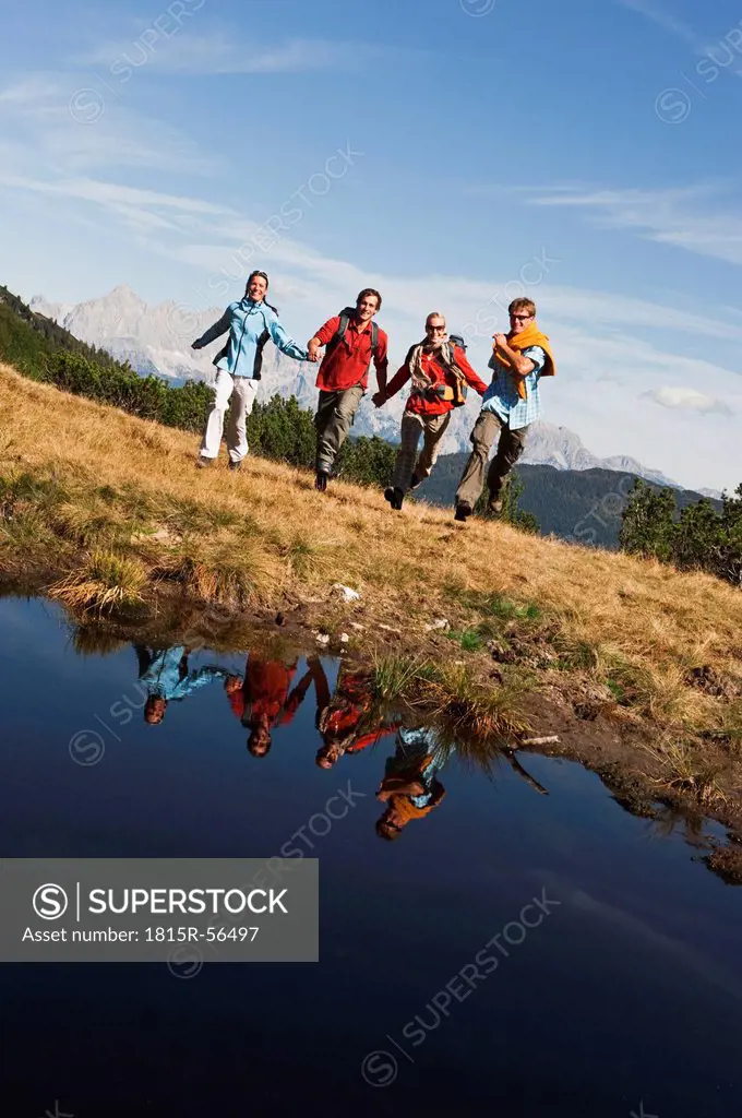 Austria, Salzburger Land, Four hikers running across field