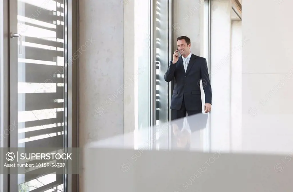 Germany, Cologne, Businessman in corridor using mobile phone