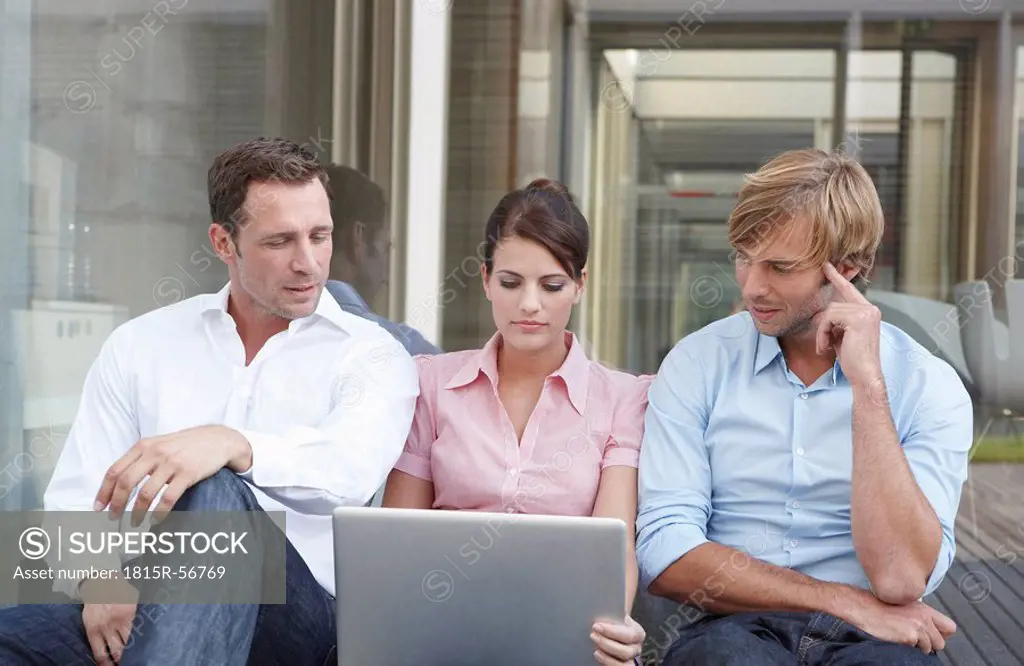 Germany, Cologne, Three business people sitting side by side, using laptop