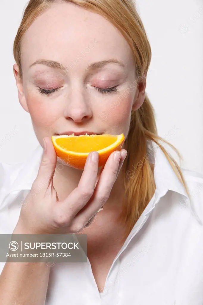 Young woman holding orange slice, eyes closed
