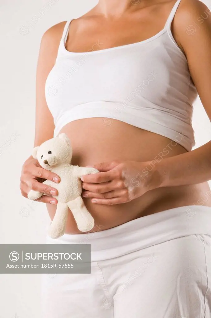 Pregnant woman holding teddy, mid section